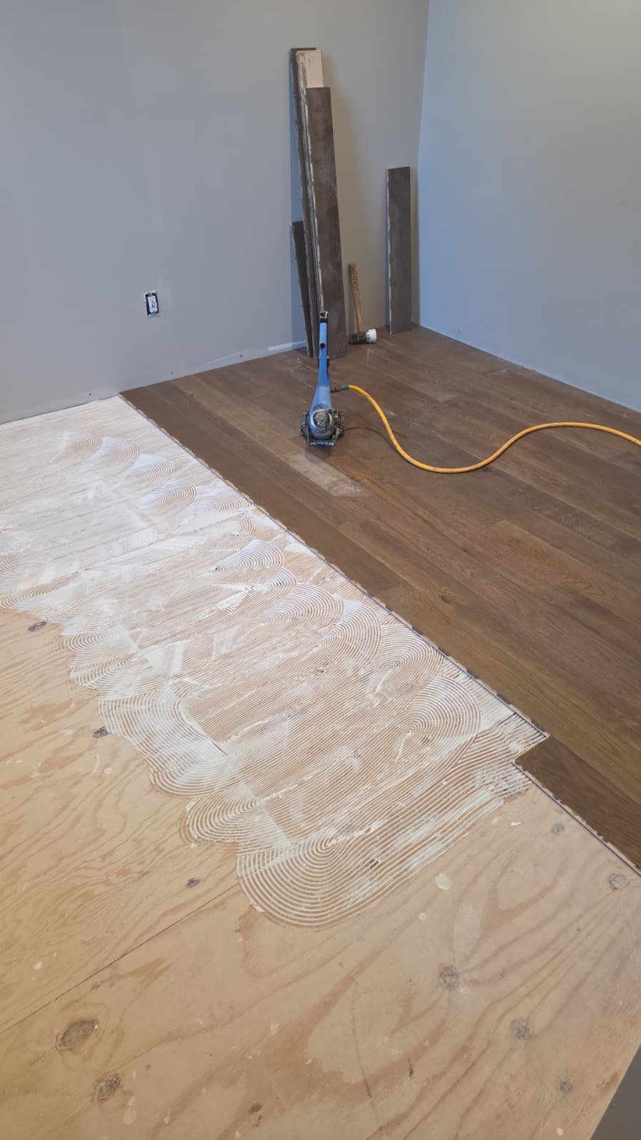 Adhesive troweled across plywood subfloor during wide plank installation